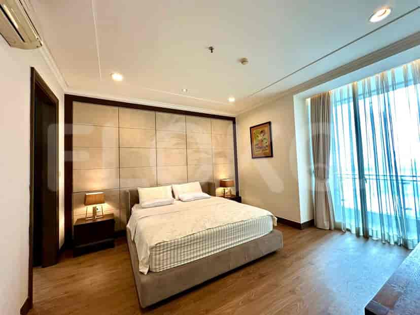 A bedroom with a king-size bed, a padded headboard, bedside tables with lamps, and a large window with sheer curtains.