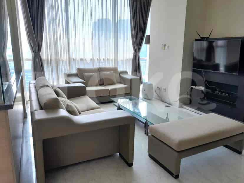 A living room with a beige sectional sofa, a glass coffee table, and a large window with sheer curtains.