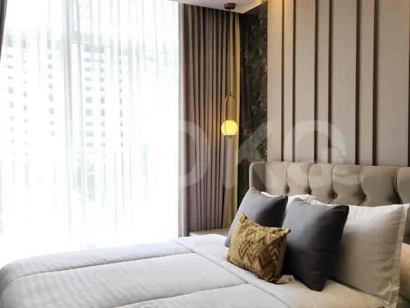 A bedroom with a large bed, upholstered headboard, and sheer curtains covering a large window.