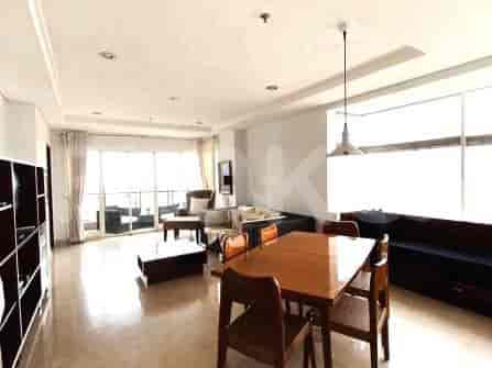 Ruang tamu dan ruang makan yang luas dengan meja makan kayu, set sofa, jendela besar, dan pencahayaan dekoratif.