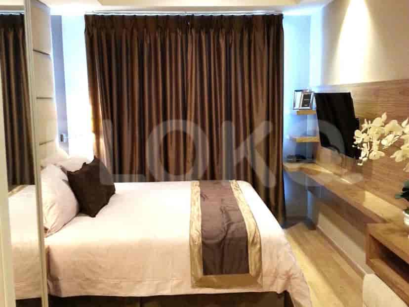 A bedroom with a bed, dark brown curtains, and a wooden vanity with a TV.