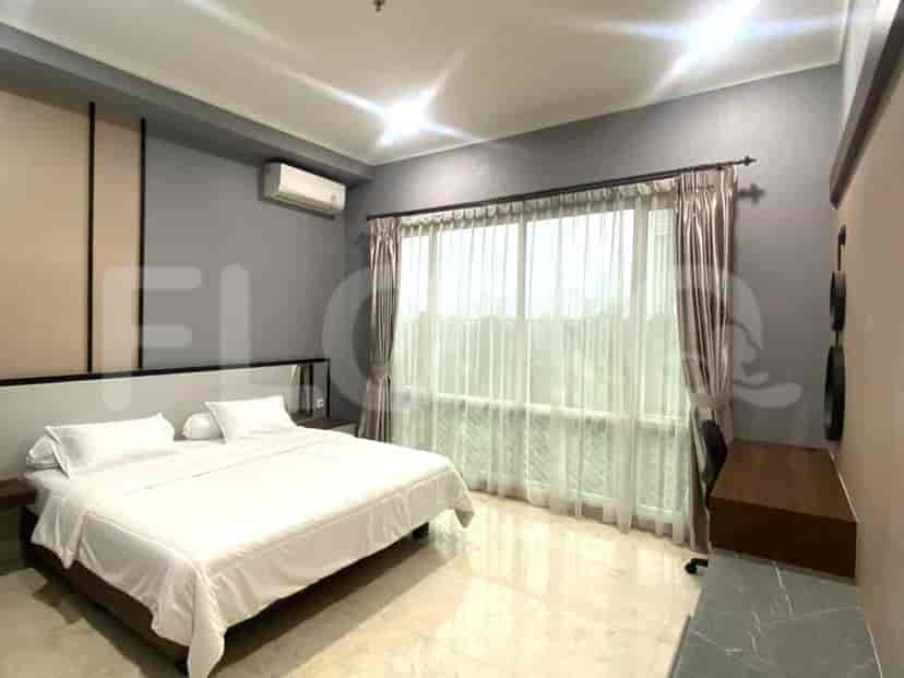 A bedroom with a king-size bed, a desk, and a large window with sheer curtains.