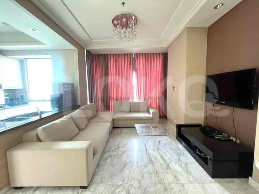 A spacious living room featuring a large L-shaped sofa, a glass coffee table, a wall-mounted TV on a black media console, and pinkish-brown curtains.