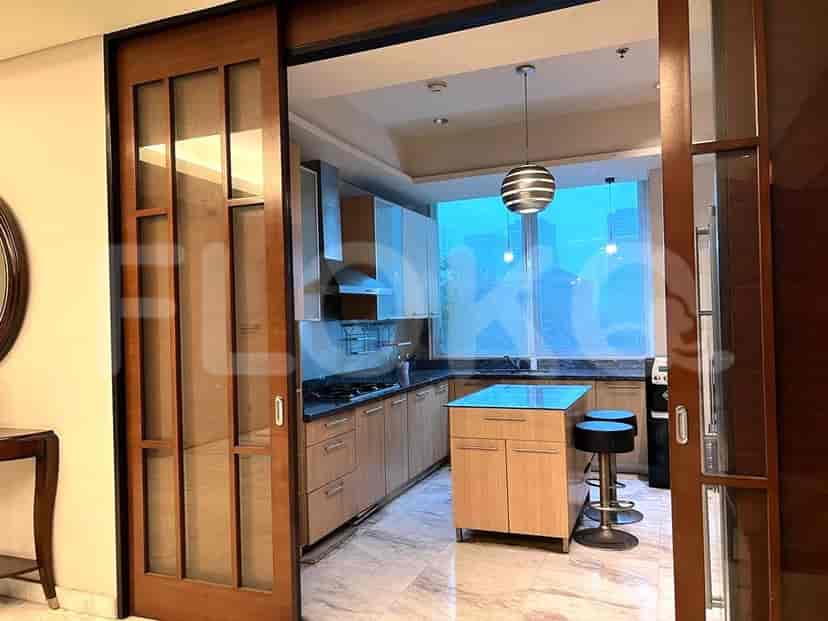 A modern kitchen with light wood cabinetry, granite countertops, a stainless steel range hood, and a central island with bar stools.