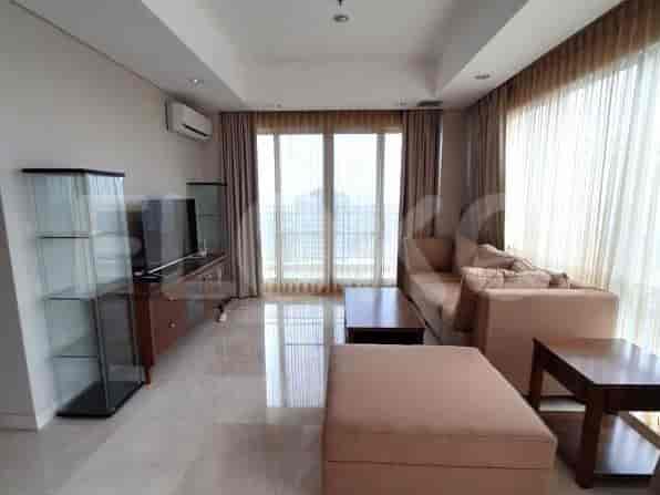 Sebuah ruang tamu terang dengan sofa besar, meja kopi, konsol TV, dan jendela dari lantai ke langit-langit.