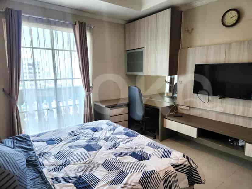 A studio apartment bedroom with a bed, desk, TV, and kitchenette area.