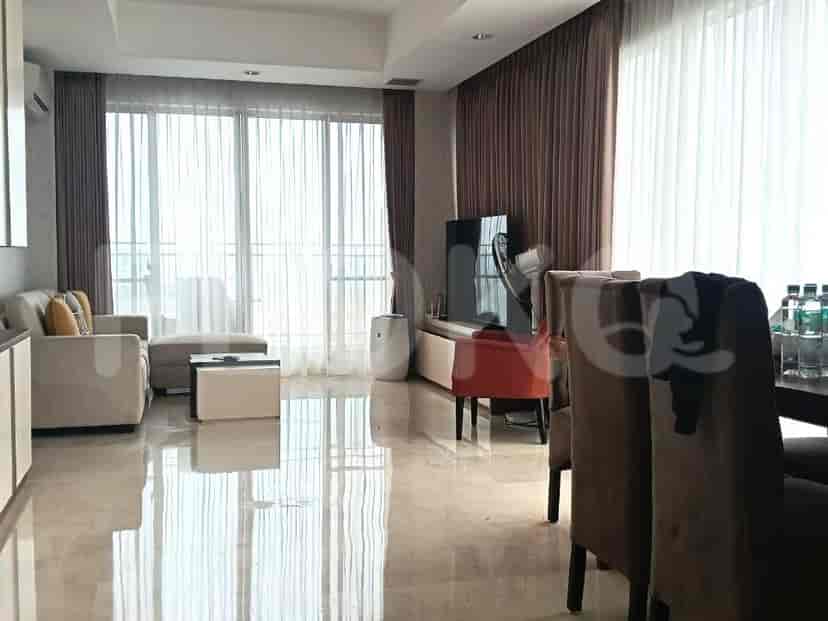 A modern living room with a light-colored sofa, ottoman, coffee table, large windows with curtains, and a TV console.