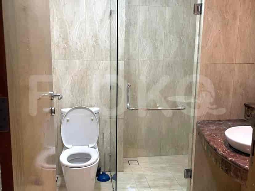 Kamar mandi menampilkan toilet modern, shower tertutup kaca dengan ubin seperti marmer, dan meja rias marmer dengan bak cuci.