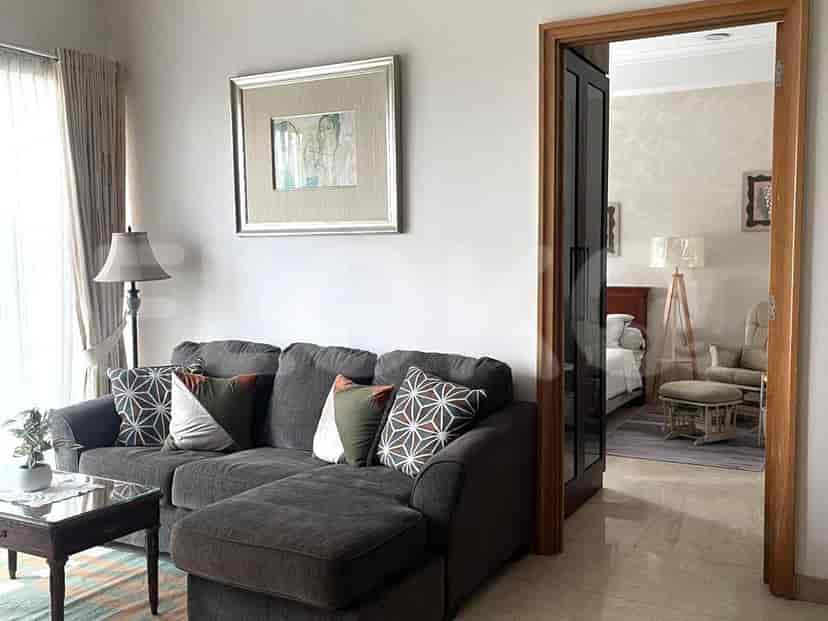 Ruang tamu yang luas menampilkan sofa sectional abu-abu gelap dengan bantal dekoratif, meja kopi berlapis kaca, dan karya seni berbingkai di dinding.
