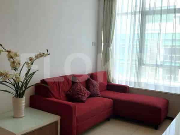 A living room with a red sectional sofa, a vase of artificial flowers, and a large window with sheer curtains.
