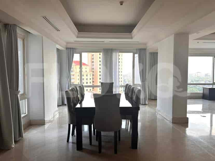 A formal dining room with a long, dark wooden table and upholstered chairs, set against a backdrop of large windows offering a city view.