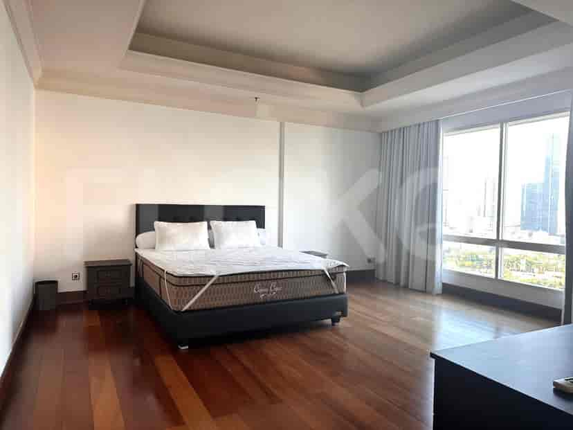 A spacious bedroom featuring a king-size bed with white linens, wooden flooring, and a large window with white curtains.