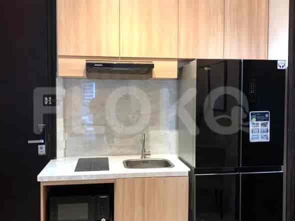 A compact kitchenette with light wood cabinets, a stainless steel sink, electric stove, and a black microwave and refrigerator.