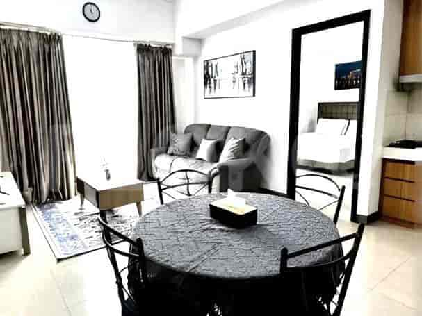 A combined living and dining area featuring a grey sofa, a round dining table with chairs, and a wall-mounted clock.