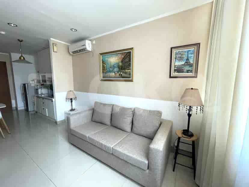 Sebuah ruang tamu modern dengan sofa, lukisan, dan lampu, bersebelahan dengan area dapur.