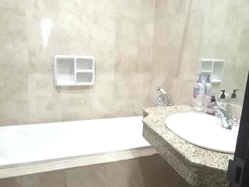 A bathroom with a bathtub, a granite-topped vanity with a sink, and marble-tiled walls.