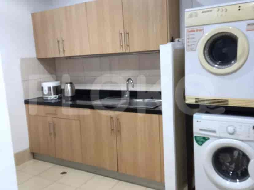 A compact utility area with light wood cabinets, a sink, a kettle, a rice cooker, a washing machine, and a dryer.
