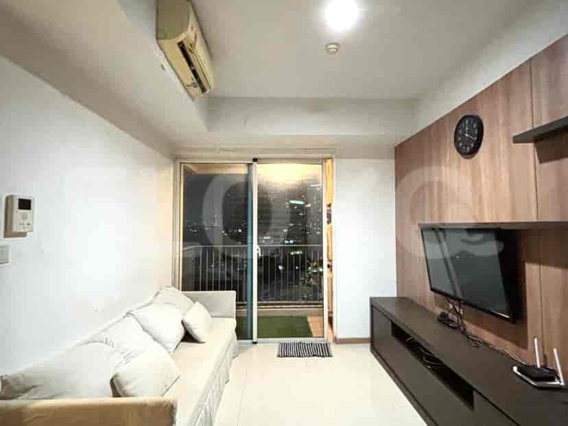 A living room with a beige sofa, a TV console with a television, and a large window overlooking a cityscape.