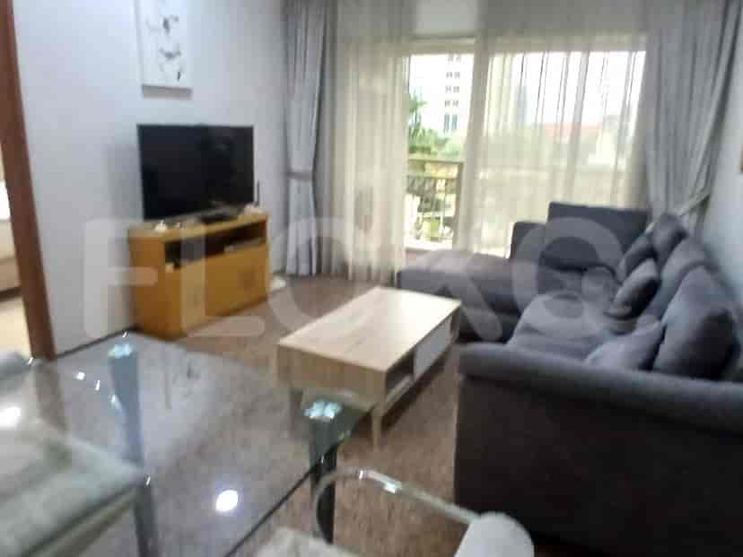 A modern living room with a grey sectional sofa, a wooden coffee table, a TV stand with a television, and large windows.