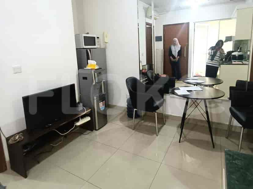 A compact living area with a black TV on a dark wooden stand, a grey refrigerator, and a black armchair.