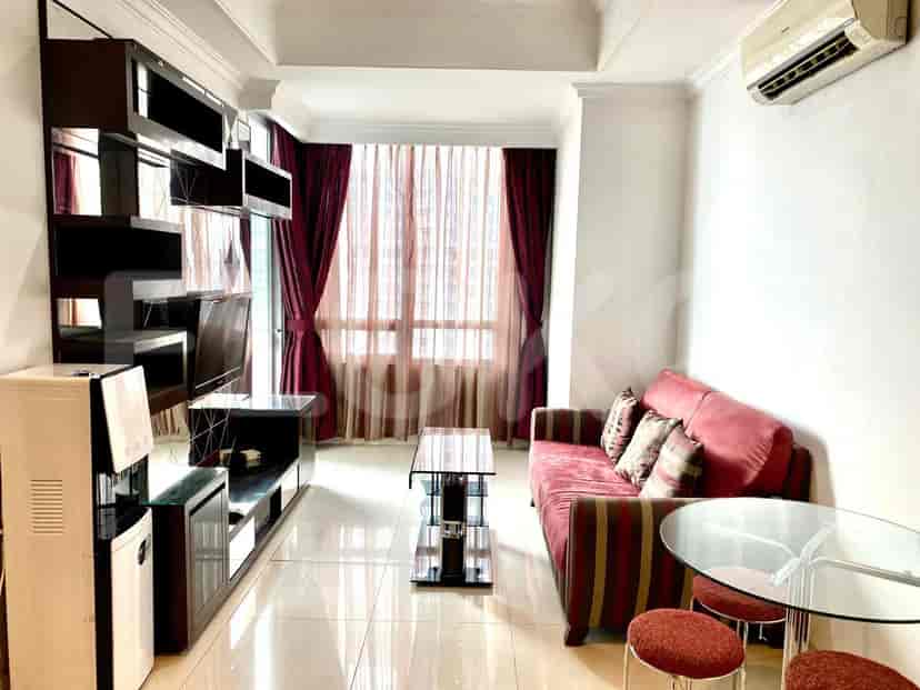 A living room with a red and striped sofa, a glass coffee table, a TV console with a water dispenser, and large windows with burgundy curtains.