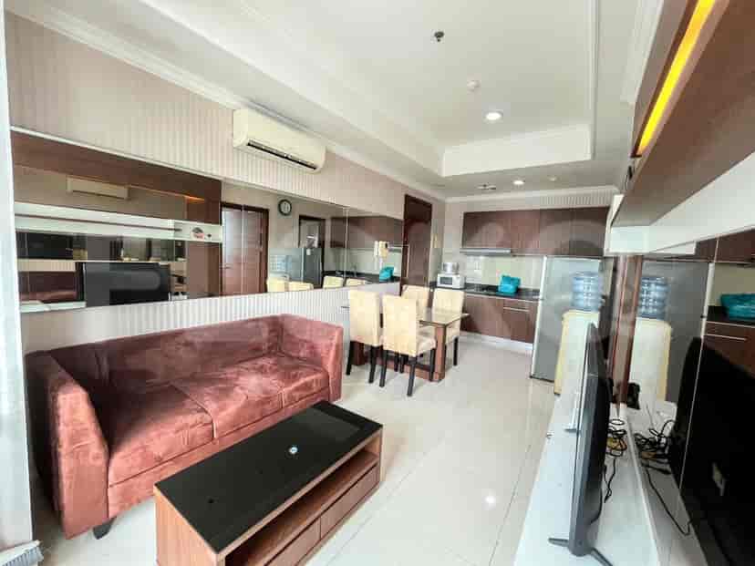 A living room with a reddish-brown sofa, a dark wood coffee table, a dining table with chairs, and a kitchen area in the background.
