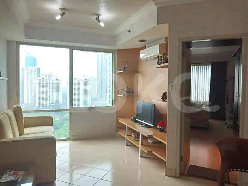 A living room with a beige sofa, a television on a wooden shelf, and large windows offering a city view.