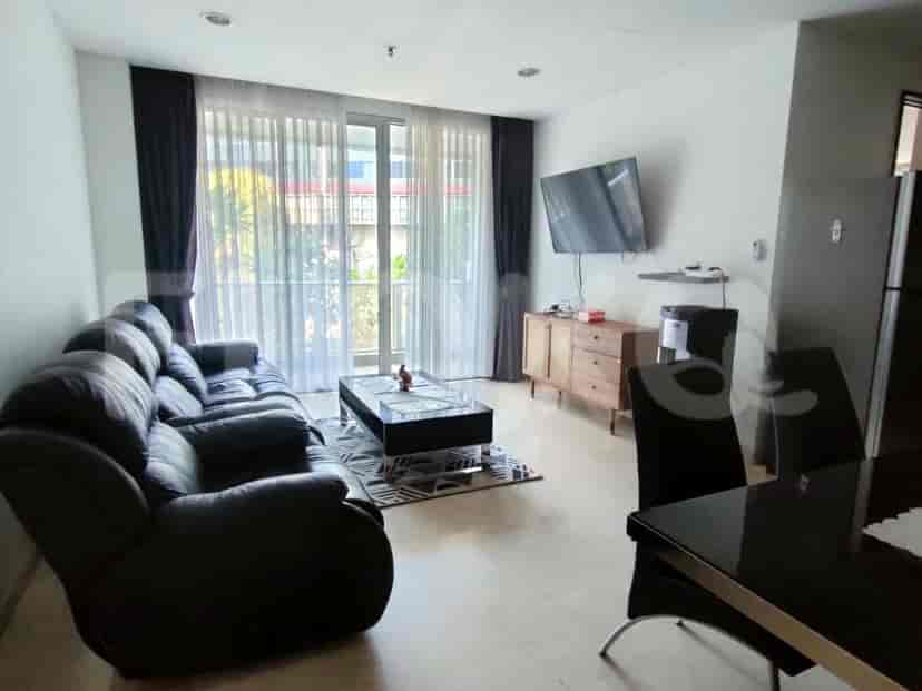 A living room featuring a black leather sofa, a glass-top coffee table on a patterned rug, and a wall-mounted TV.