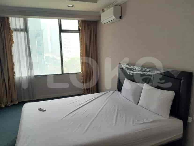 A bedroom with a queen-sized bed, white linens, and large windows with beige curtains.