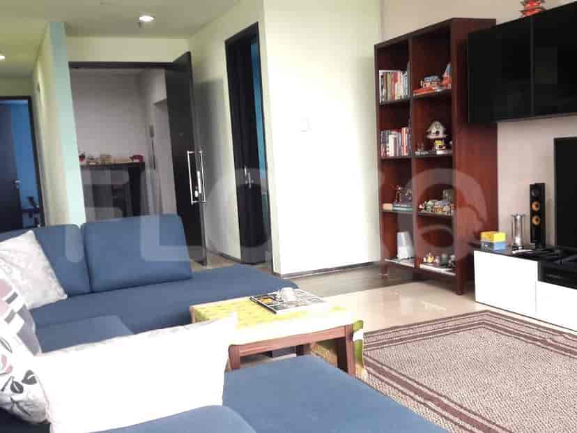 A living room with a large blue sectional sofa, a coffee table, a bookshelf, and a wall-mounted TV.