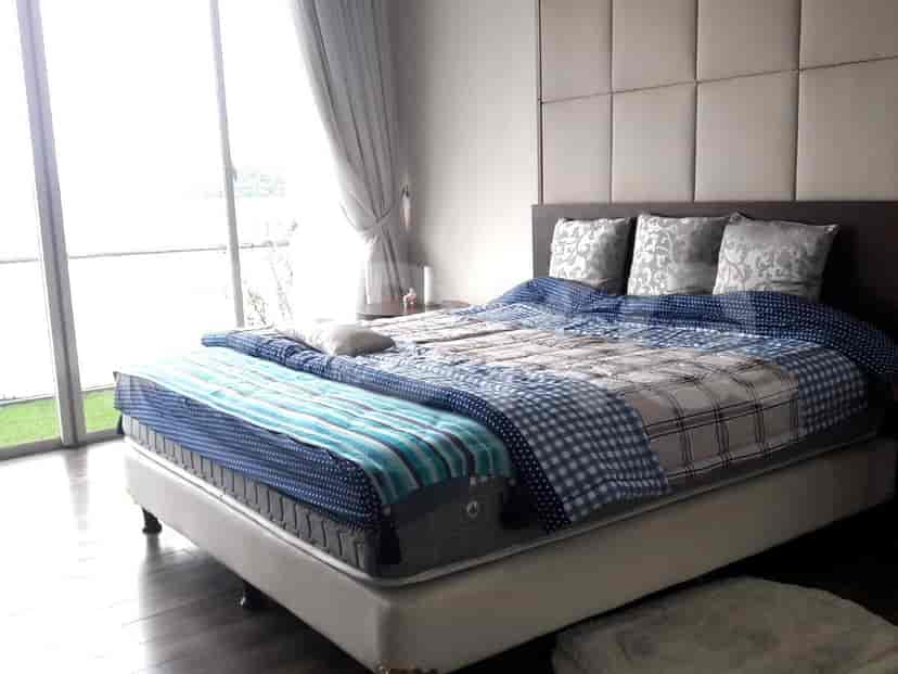 A bedroom with a large bed, large windows with sheer curtains, and a padded headboard.