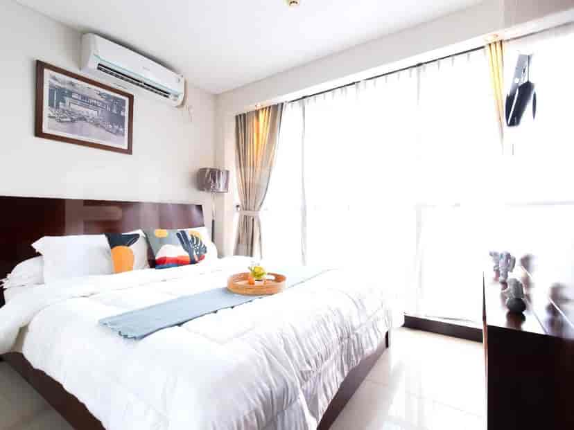 A bedroom with a large bed, an air conditioner, and a window with sheer curtains.
