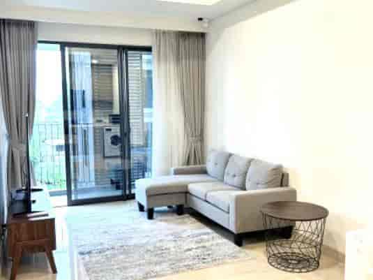 Ruang tamu terang dengan sofa sudut abu-abu, meja kopi, dan balkon yang dapat diakses melalui pintu kaca.