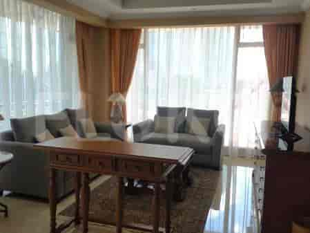 A living room with a large L-shaped sofa, a wooden console table, a patterned rug, and sheer curtains.
