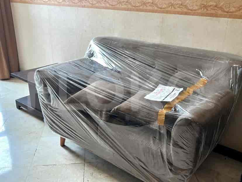 Sofa yang ditutupi plastik, dengan meja kopi di belakangnya.