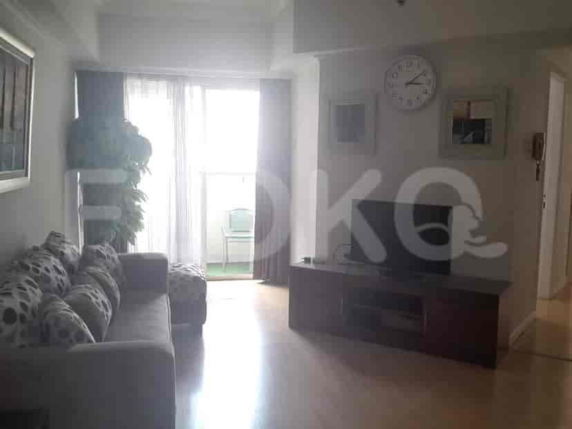 A living room with a sofa, ottoman, TV stand, and a large window with curtains.