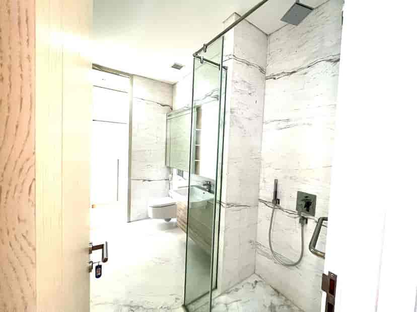 Kamar mandi modern dengan ubin bermotif marmer, shower kaca, dan meja rias.