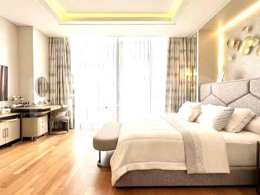 A luxurious master bedroom with a large bed, a vanity area, and a view through large windows.