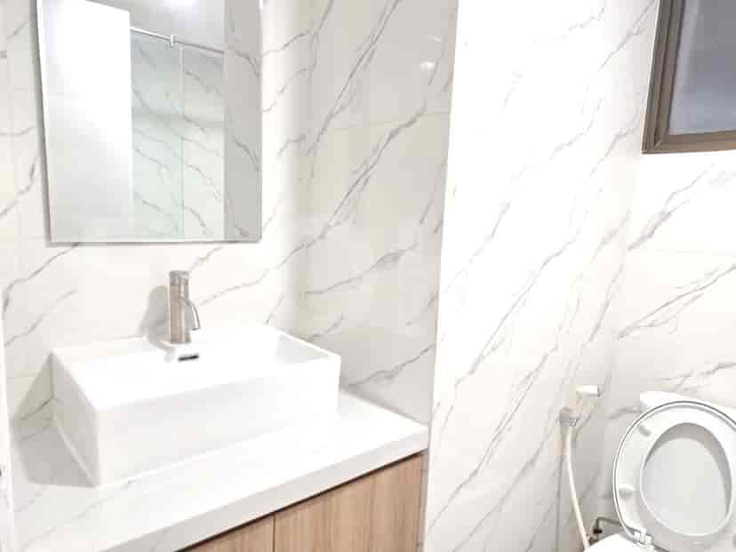 Sebuah kamar mandi dengan wastafel, keran, dan toilet, menampilkan dinding bermotif marmer putih.
