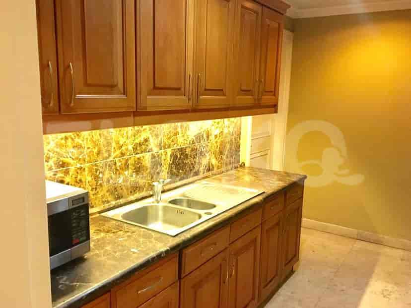 A compact kitchenette with wooden cabinets, a double sink, and a microwave.