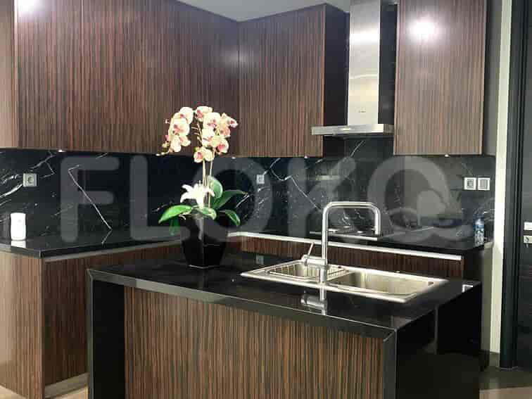 A modern kitchen with dark wood cabinets, a black countertop, and a stainless steel sink.