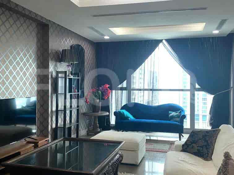 A luxurious living room with a blue velvet sofa, ornate coffee table, and large windows with dark curtains.