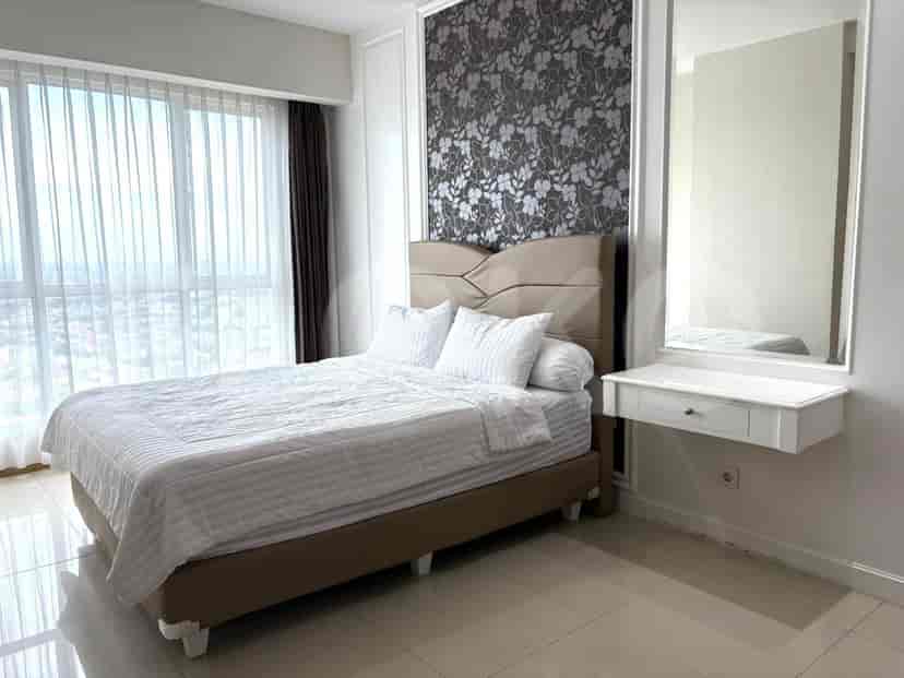 A bedroom with a king-size bed, a dresser with a mirror, and large windows.