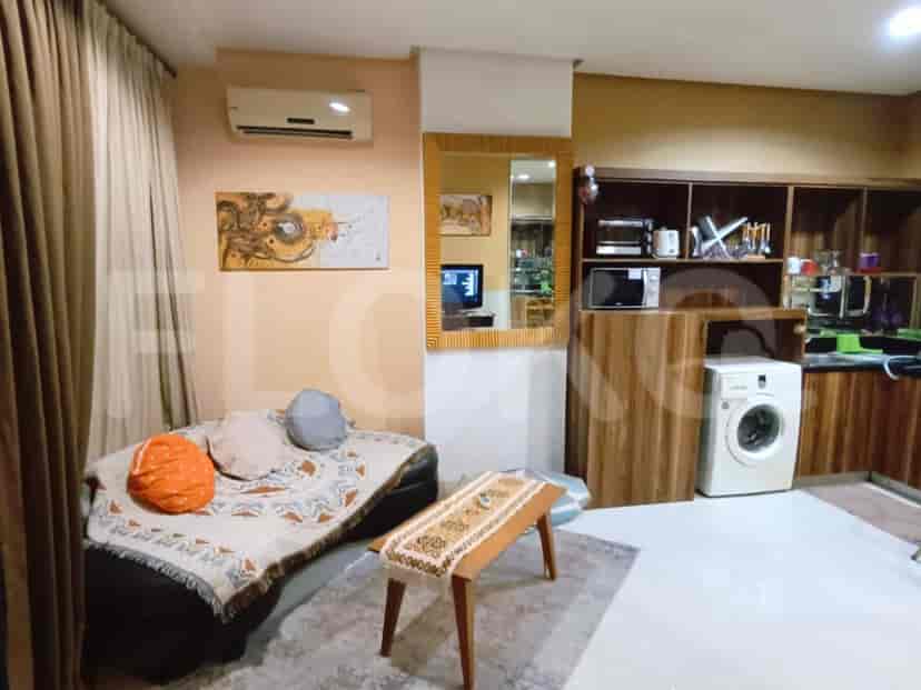 A compact living area with a dark sofa, colorful cushions, a wooden coffee table, and a large mirror reflecting kitchen appliances.