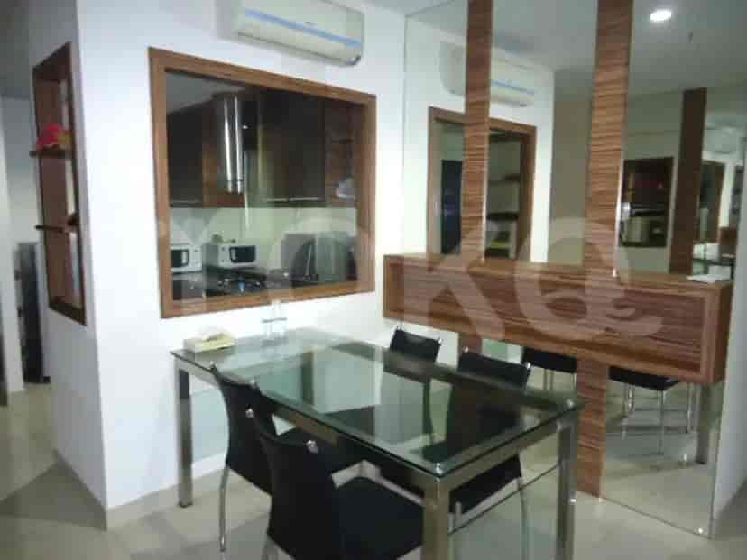 Area makan dengan meja kaca dan kursi, bersebelahan dengan dapur terbuka.