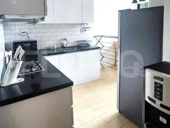 Dapur ringkas dengan lemari putih, meja hitam, kompor gas, microwave, dan kulkas.