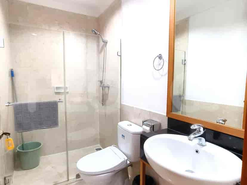 A modern bathroom with a walk-in shower with a glass enclosure, a toilet, and a vanity with a white sink and a wooden-framed mirror.