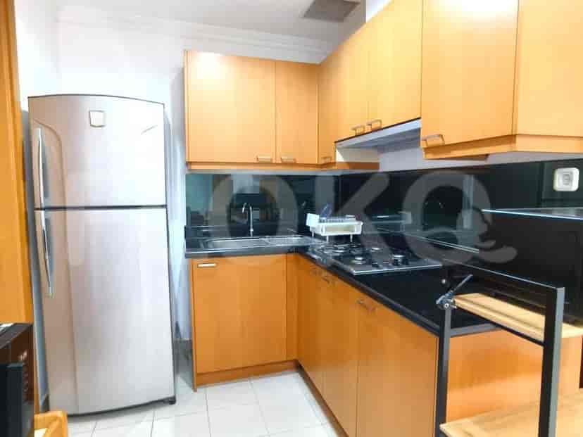 A compact kitchen with light wood cabinets, a stainless steel refrigerator, a black countertop with a sink and stove, and a black backsplash.