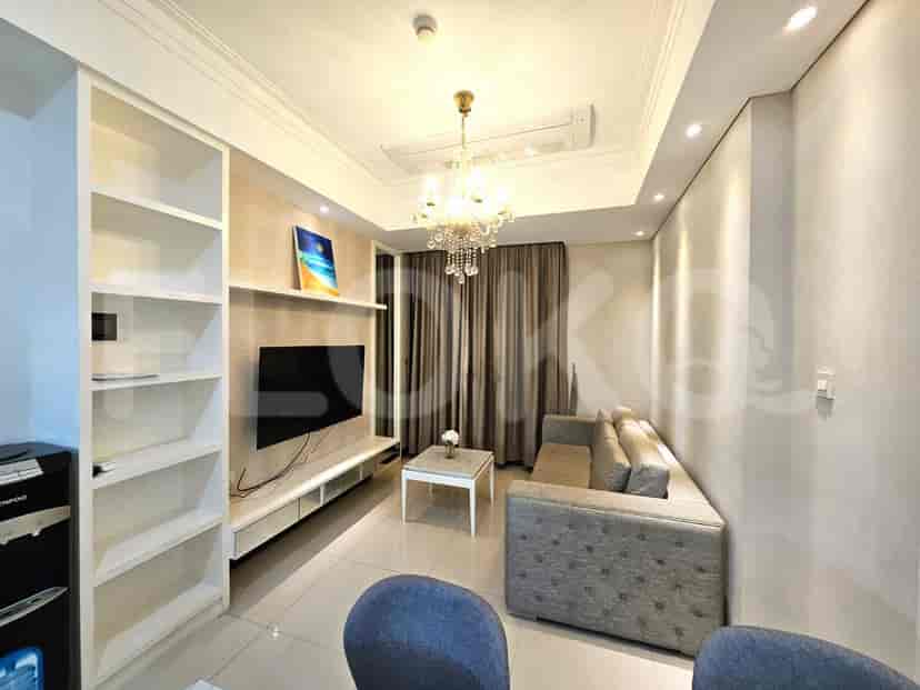 Sebuah ruang tamu dengan sofa sectional, TV besar, rak buku, dan lampu gantung.