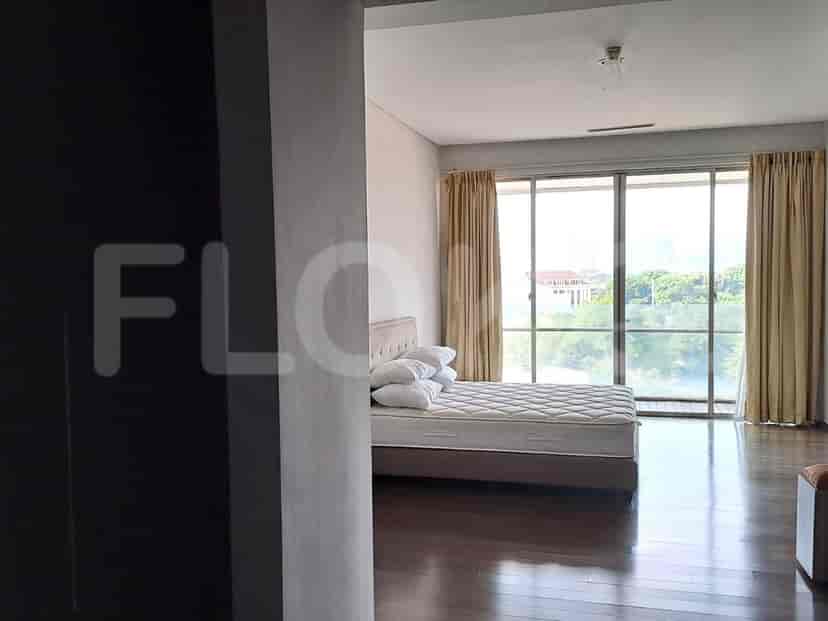 A bedroom with a mattress on a bed frame, pillows, and large glass windows with curtains.